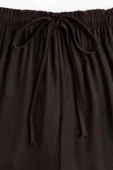 Pantalón marrón oscuro de corte holgado y piernas amplias, con cintura elástica fruncida y cordón ajustable.