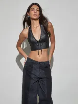 Top halter de cuero sintético negro con escote en V profundo, detalles de ojales metálicos y cordón ajustable frontal.