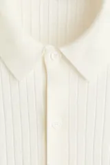 Camisa de punto acanalado color blanco, con cuello camisero, manga corta y cierre frontal con botones.