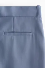 Pantalón sastrero de sarga color azul, de corte recto y pierna ancha, con pliegues frontales y doblez ancho en los bajos.