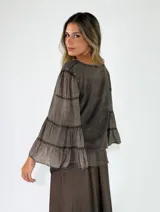 Blusa de algodón color gris oscuro con efecto gastado, mangas largas amplias con múltiples volados escalonados y terminaciones deshilachadas.