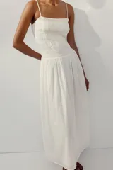 Vestido midi de color blanco con escote recto y tirantes finos ajustables. Presenta un cuerpo con tejido elástico tipo nido de abeja y detalles de flores bordadas en la parte superior. Cuenta con bolsillos laterales ocultos y forro interior.
