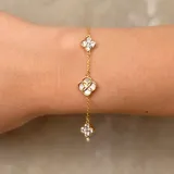 Pulsera de cadena fina dorada con tres dijes en forma de flor. El dije central presenta un diseño calado con incrustaciones de nácar y un pequeño cristal, mientras que los dos dijes laterales están completamente cubiertos de cristales brillantes.