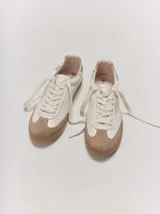 Championes de cuero color blanco con puntera y suela de goma marrón claro. Presentan detalles bordados dorados en los laterales y cordones anchos en color crudo.