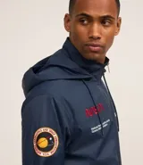 Campera rompevientos azul marino con capucha, cierre frontal y bolsillos laterales. Presenta estampado de NASA en el pecho, parche de bandera estadounidense en la manga y bolsillo utilitario en el brazo.