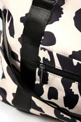 Bolso tipo duffel con estampado animal print en tonos crema y negro. Cuenta con correas de mano y correa ajustable para el hombro en color negro, cierre principal superior y bolsillo frontal con cierre.