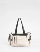 Cartera tipo bolso color beige con detalles en negro, confeccionada en nylon. Presenta múltiples compartimentos externos, incluyendo bolsillos laterales removibles, cierre superior y correas de hombro resistentes.