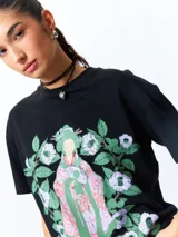 Remera negra de manga corta, corte oversize, con estampado frontal de una figura femenina de estilo asiático rodeada de flores blancas y verdes.