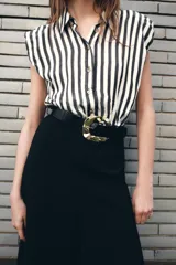 Vestido midi de diseño combinado con cuerpo de camisa sin mangas a rayas verticales en blanco y negro, y falda negra de corte recto. Presenta cuello solapa, cierre frontal con botones y cinturón negro con hebilla metálica dorada.