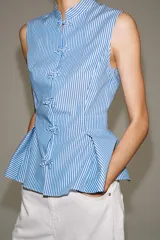 Camisa sin mangas de algodón con rayas verticales blancas y azules, cuello mao, bajo acabado en peplum y cierre frontal con alamares decorativos de nudo.