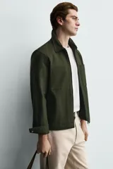 Sobrecamisa negra de corte relajado, confeccionada en tejido con mezcla de algodón elástico. Presenta cuello solapa, cierre frontal de cremallera, bolsillos de plastrón en el pecho y bolsillos de vivo en la cadera.