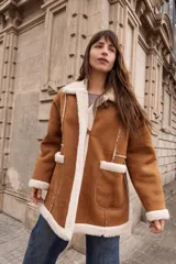 Tapado estilo gamulán con interior de corderito sintético, cuello amplio, bolsillos delanteros y cierre frontal con alamares. Diseño de corte oversized con terminaciones a contratono.