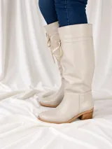 Bota de caña alta confeccionada en napa, con diseño de caña caída y detalle de cordones laterales para ajuste. Cuenta con taco cuadrado foliado de 4,5 cm y suela de goma antideslizante.