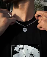 Cadena plateada de eslabones finos con dije circular con diseño de rosa de los vientos.