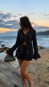 Blusa negra de manga larga acampanada con detalles de encaje y cierre frontal con tiras para anudar.