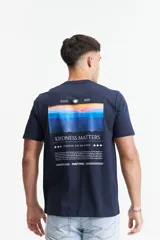 Remera de manga corta color azul marino con cuello redondo y calce regular. Presenta un estampado gráfico en la espalda que incluye un paisaje montañoso al atardecer, el texto 'KINDNESS MATTERS' y el logo de la marca Mistral.