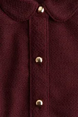 Vestido corto de tejido bouclé color bordó, con corte evasé, cuello camisero y tapeta de botones dorados. Posee mangas cortas y costuras princesa tanto adelante como atrás.