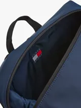 Mochila azul marino con acabado liso, compartimento principal con cierre de cremallera, bolsillo frontal vertical con cremallera, dos bolsillos laterales para botellas y correas ajustables. Incluye parche engomado con el logo de Tommy Jeans en la parte delantera.