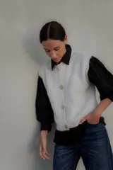 Chaleco de punto en color marrón oscuro, con cuello redondo y cierre frontal mediante botones metálicos decorativos con forma de sol.