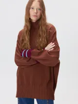 Pullover de punto color rojo, con cuello tortuga, corte holgado y mangas largas con puños acanalados en contraste con rayas blancas. Presenta un logo bordado en el pecho.