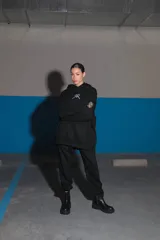 Buzo negro oversize de frisa con capucha amplia, bolsillo canguro, terminaciones de puño y ruedo con rib, y logo bordado en el centro delantero.