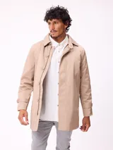Gabardina de corte clásico en color beige, con cierre frontal de cremallera y botones, cuello camisero y puños ajustables con trabillas.