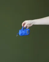 Charm en forma de mini bolso azul, con asas superiores y gancho tipo mosquetón, confeccionado en tela con etiqueta de la marca.
