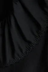 Blusa negra de viscosa con cuello Peter Pan fruncido y ribete de encaje. Presenta cierre frontal con tiras para anudar, mangas cortas abullonadas y puños con elástico.