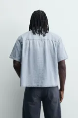 Camisa de corte boxy fit confeccionada en denim ligero de algodón. Presenta cuello solapa, manga corta y cierre frontal con botones. Diseño con efecto lavado.