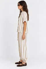 Pantalón a rayas beige y blancas con cintura elástica, bolsillos laterales y traseros, corte holgado con piernas globo y cordón de ajuste en los tobillos.