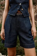 Shorts de denim azul oscuro, tiro alto, con pinzas delanteras y corte ancho. Incluye un cinturón fino marrón con hebilla de eslabones dorados.
