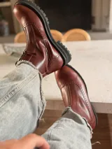 Botas de cuero color marrón rojizo con diseño estilo brogue, cierre lateral y suela track negra de goma resistente.