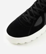 Championes de corte medio confeccionados en poliuretano negro, con diseño de paneles combinados y perforaciones laterales. Presentan cierre con cordones y una suela track alta de color blanco con relieve.