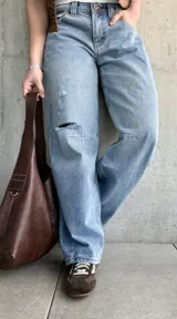 Jean de denim celeste de corte barrel, tiro bajo, con roturas y detalles desgastados en la rodilla.