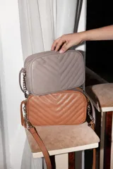 Cartera bandolera negra con diseño capitoneado en forma de V, correa de cuero y cadena plateada, cierre metálico y doble bolsillo interior.