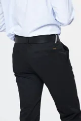 Pantalón de vestir negro, de gabardina, con corte clásico, bolsillos laterales y traseros con botón. Se ajusta a la cintura con cinturón de cuero negro.