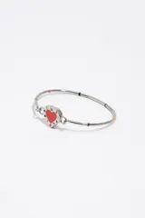 Pulsera rígida de metal plateado con dije central en forma de corazón esmaltado en color rojo y blanco, con letras grabadas alrededor.