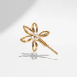 Broche en forma de flor elaborado en acero dorado, con pétalos de alambre trenzado y centro decorado con perlas.