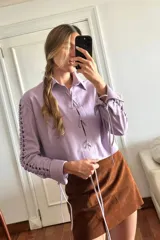 Camisa de cuero ovino desgastado color lila, con escote en V y cordones cruzados en el centro. Presenta mangas largas con recortes y cordones decorativos a lo largo de los brazos.