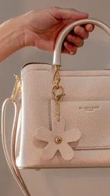 Cartera tipo tote color bordó, con doble asa corta y correa larga desmontable. Tiene bolsillo externo con solapa y dije colgante en forma de flor.