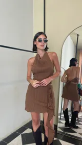 Pollera corta color marrón, confeccionada en crepé texturado con elasticidad. Presenta un diseño con volado lateral asimétrico que cae en cascada y detalles verticales en la textura de la tela.