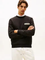 Buzo de cuello redondo Tommy Hilfiger de color negro, confeccionado en tejido interlock técnico de algodón y poliéster. Presenta corte regular, puños y bajo de punto canalé, con un parche bordado del logo de la marca en el pecho y la bandera distintiva bordada en el puño.