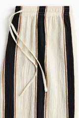 Pantalón de punto de corte holgado con piernas amplias y tiro alto, cintura elástica con cordón de ajuste y diseño a rayas verticales en tonos blanco, negro y marrón.