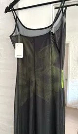 Vestido largo de microtul negro con estampado de flores grandes en tonos verdes. Presenta breteles finos, escote redondo y diseño ajustado al cuerpo con transparencias.