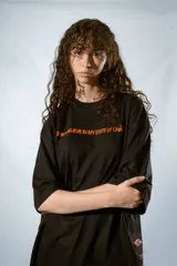 Remera negra de corte holgado con mangas cortas y estampado en color naranja con la frase "Don't believe in my state of cha..."