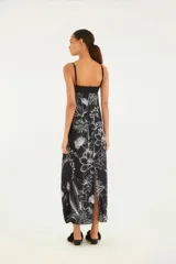 Vestido largo con estampado floral blanco sobre fondo negro, con breteles finos y escote recto. Presenta un corte en la zona del busto con abertura central.