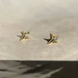 Par de aros dorados con forma de estrella fugaz y un pequeño cristal engarzado en el centro.