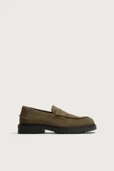 Mocasines de vestir color marrón oscuro, confeccionados en piel con acabado en gamuja serraje. Presentan detalle de antifaz en el empeine con costuras pespunteadas, punta redonda y suela track de goma robusta.