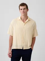 Camisa de manga corta color beige claro, con cuello cubano y cierre frontal de botones.