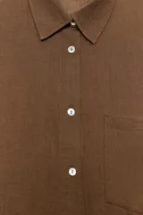 Camisa de corte oversize con cuello solapa, manga larga con hombro caído y puños. Presenta un bolsillo de plastrón en el frente, pinza en la espalda y cierre frontal con botones.